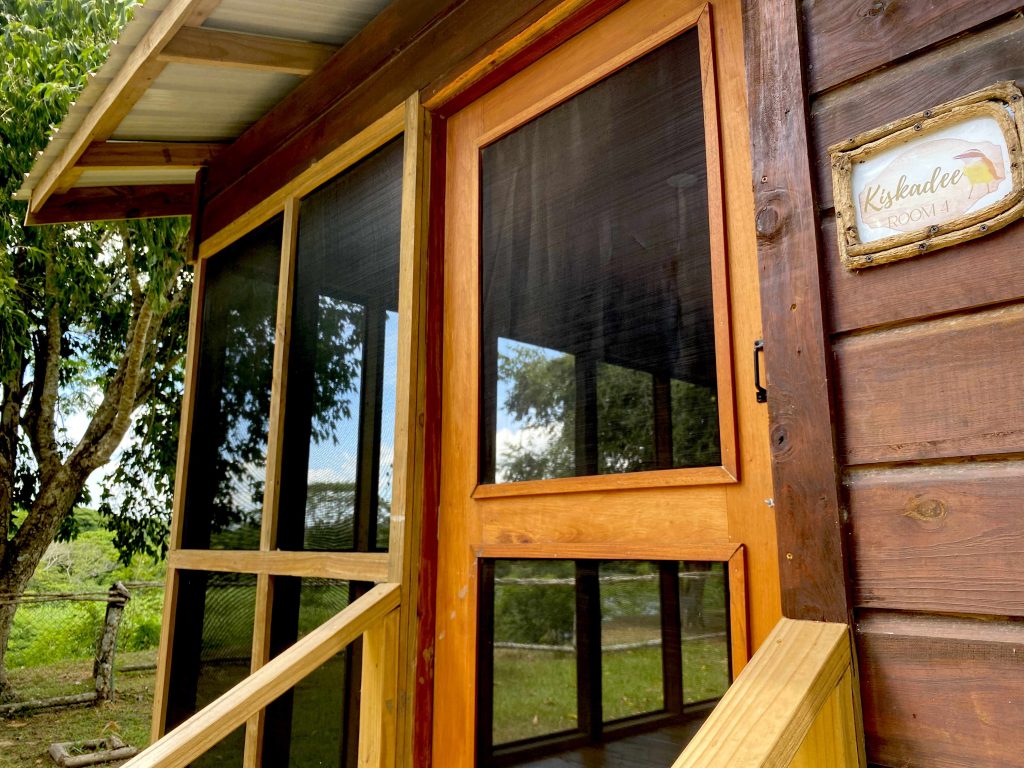 Close-up view of the Kiskadee Cabin entrance at Cahal Pech Cabins in Carmelita, showing the screened veranda and cabin name sign.